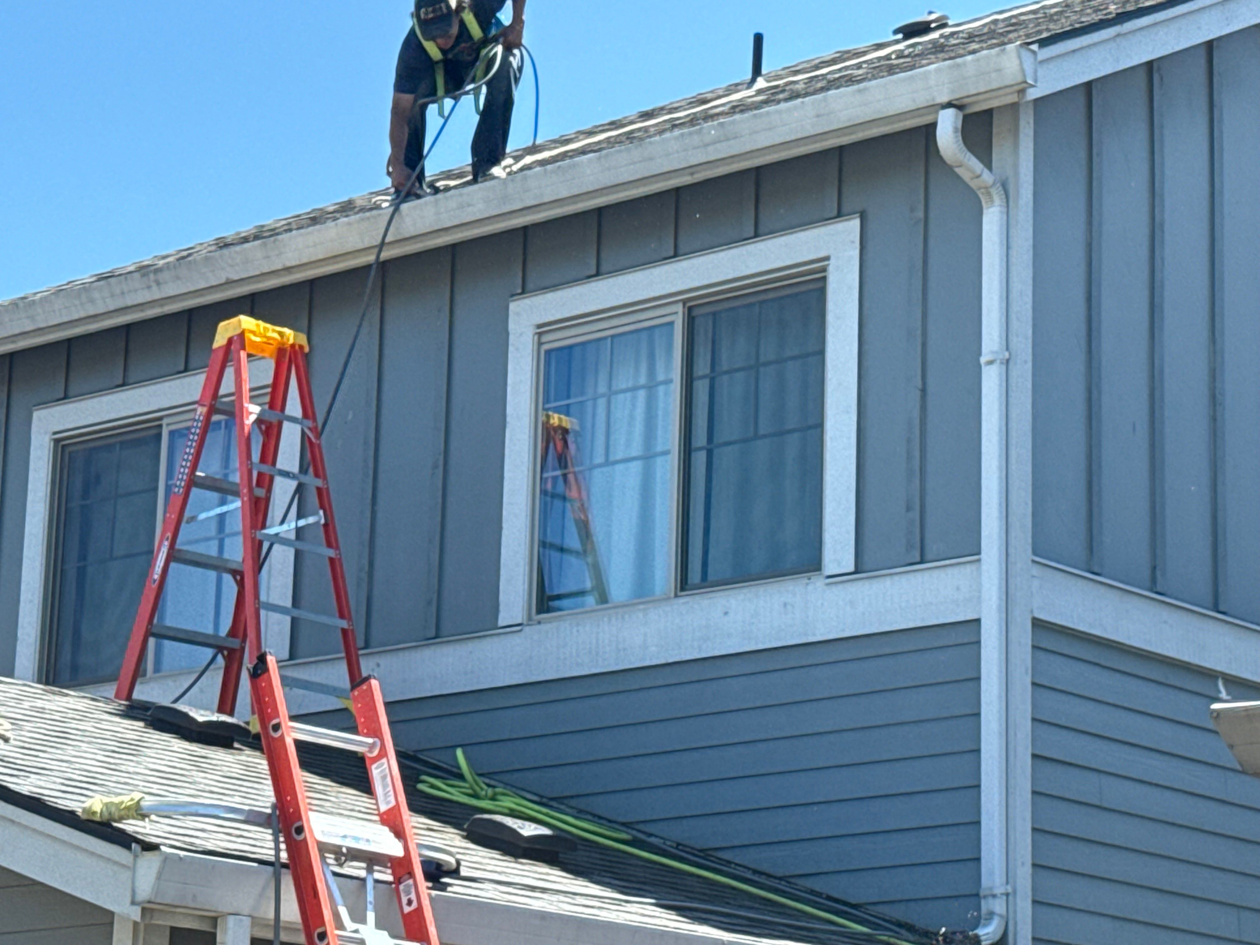 An exterior Cceaning professional performing house washing services on top of a roof